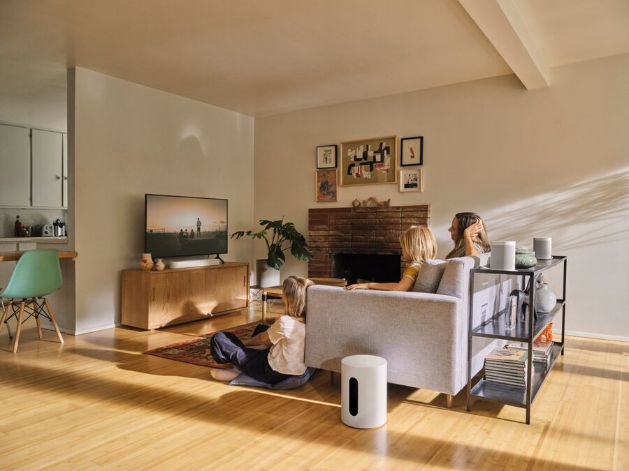 A family sitting in a media room with a TV and several Sonos whole-home speakers in the space.